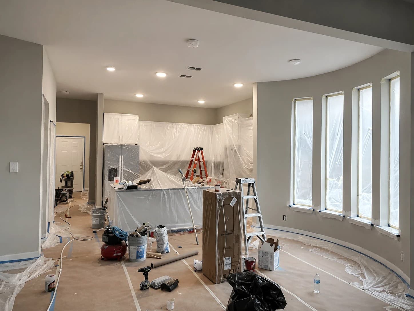 Interior painting in progress by REVIBE REMODELING — freshly coated walls with the cabinets, floors, and windows carefully masked and protected with plastic and painter's tape.