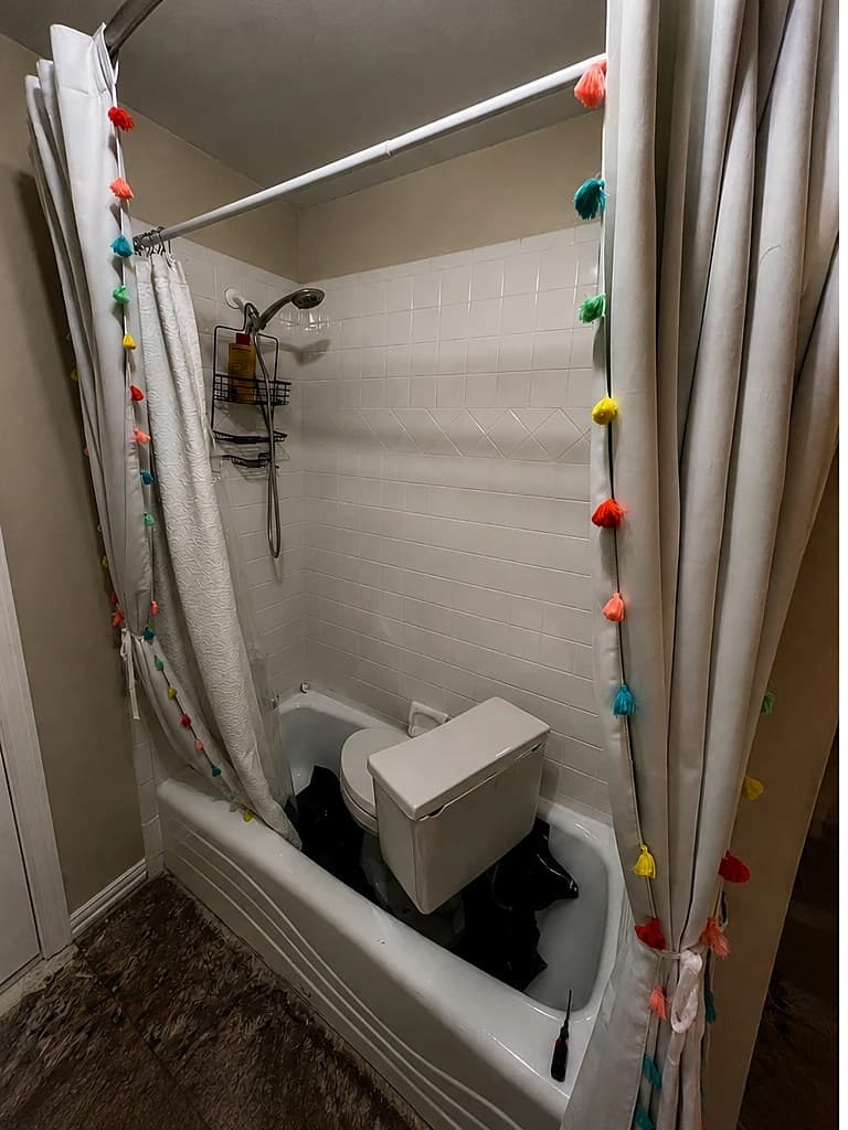 Bathroom before remodeling — a dated white-tiled tub-and-shower with a shower curtain.