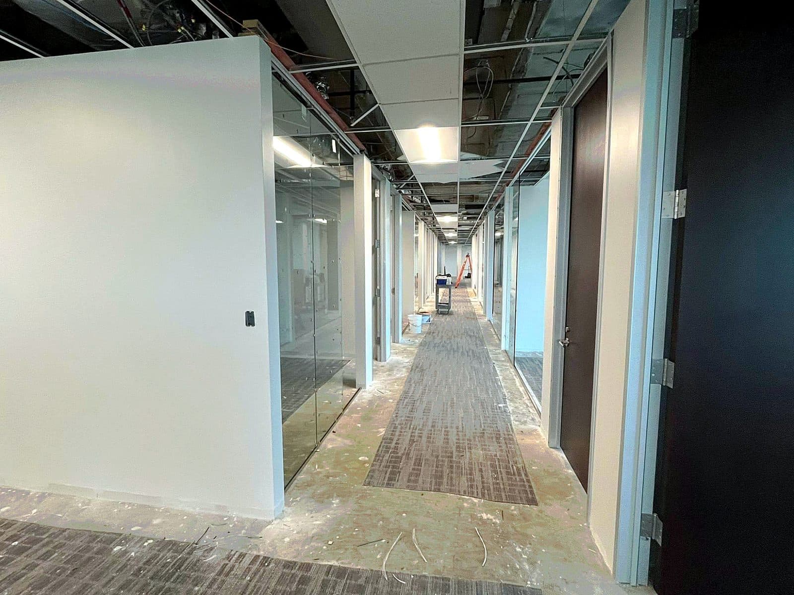 Commercial office corridor under construction by REVIBE REMODELING — glass partition storefronts and a suspended ceiling grid taking shape during a tenant build-out.