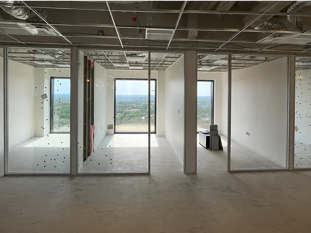 The same floor framed out — metal-stud office partitions with drywall and a suspended ceiling grid taking shape, framing floor-to-ceiling window views.