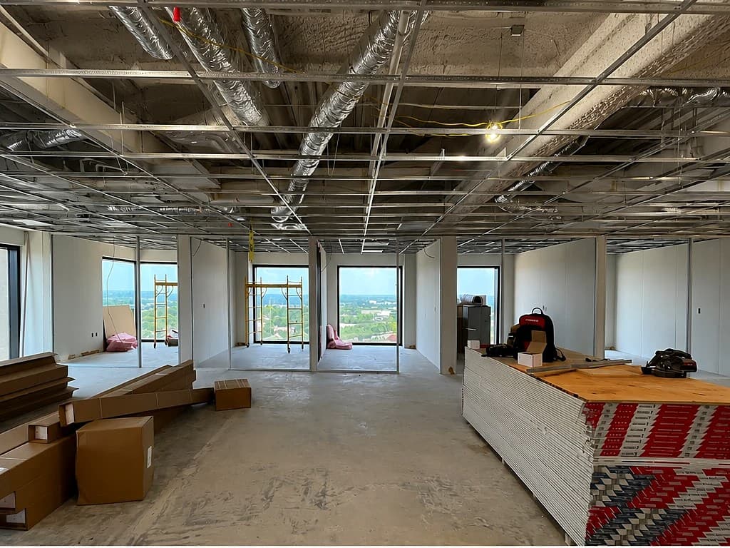 Bare commercial floor before build-out — exposed ceiling and ductwork, concrete floor, and stacked drywall waiting to be hung.